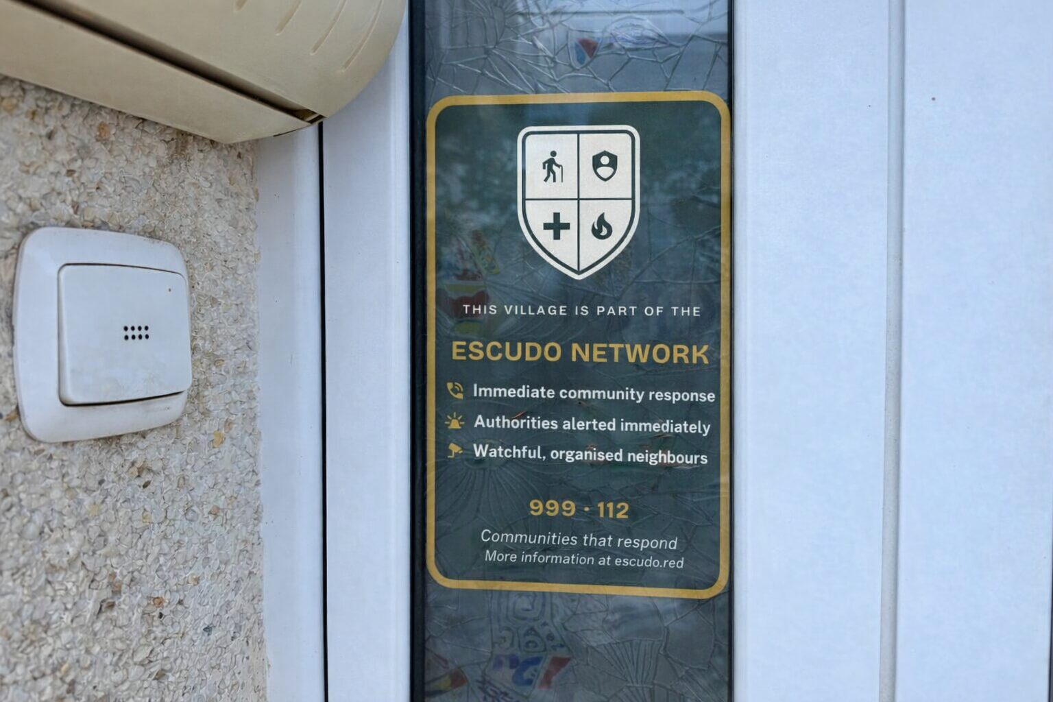 Escudo sticker on the glass of a front door, next to the doorbell.