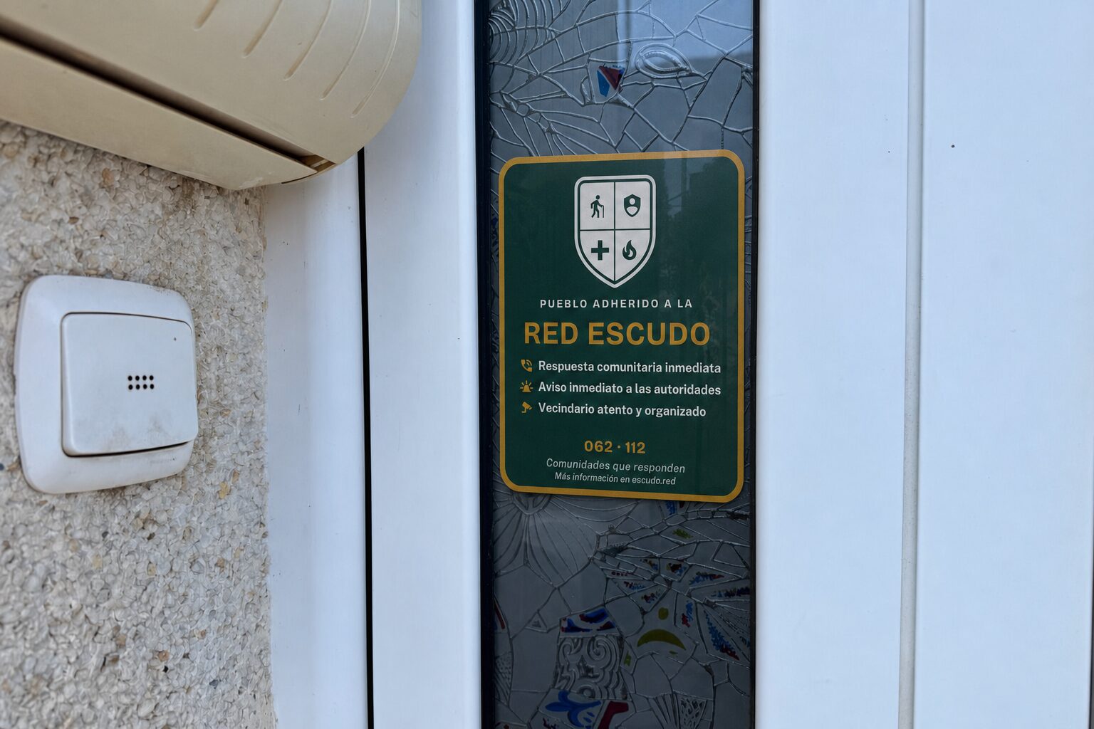 Pegatina Escudo colocada en el cristal de una puerta de entrada, junto al timbre.